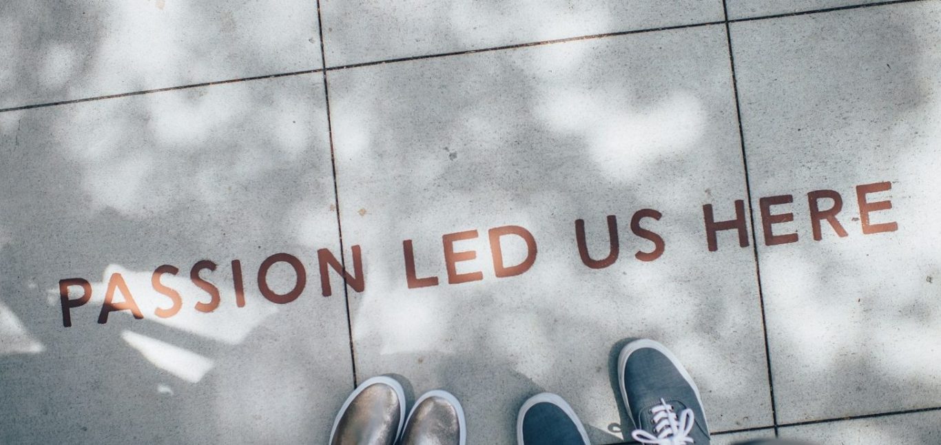 Quote on ground. Text on pavement reads "PASSION LED US HERE" with two pairs of feet visible.